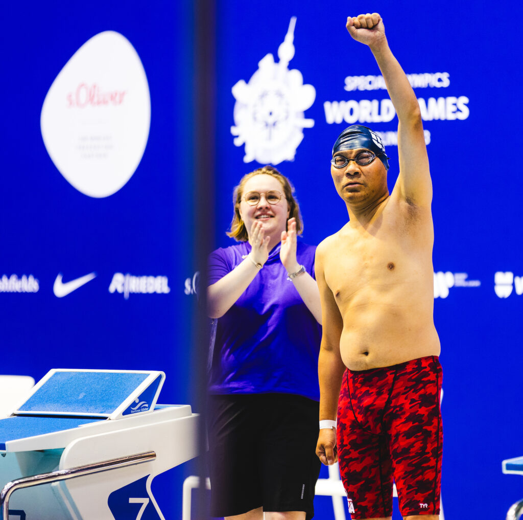 athlete raises fist before swim race as official cheers on